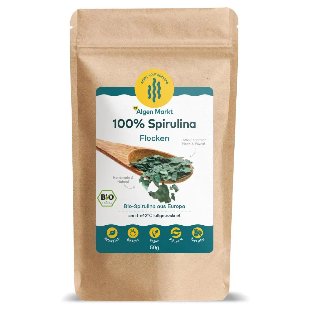 Bio Spirulina Flocken 50g von Algenmarkt – grüne Algenflocken auf Holzlöffel vor Kraftpapierbeutel