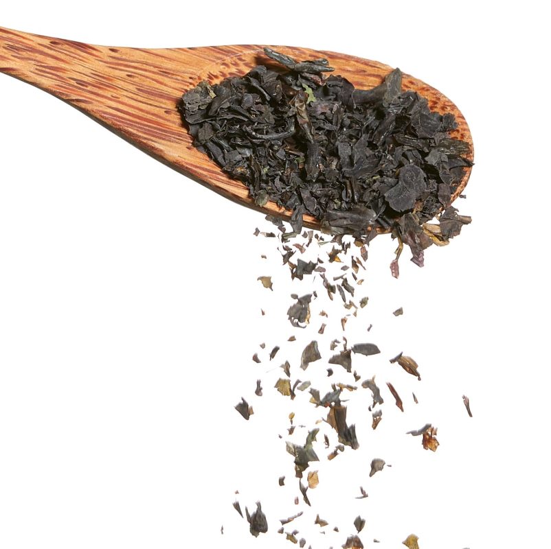 Holzlöffel mit dunklen Bio Nori Algenflocken von Algenmarkt vor weißem Hintergrund