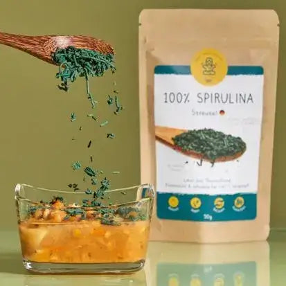 Spirulina-Streusel von Algenmarkt werden aus Holzlöffel über eine Schale gestreut